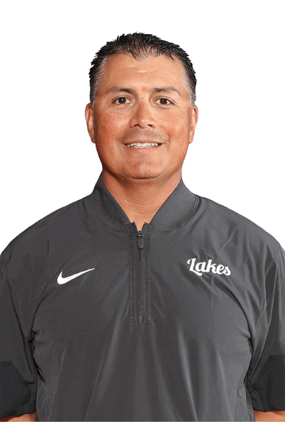 A person with short dark hair is wearing a dark gray Nike quarter-zip shirt with the word “Lakes" embroidered on the chest, smiling against a plain light background. Description generated by AI