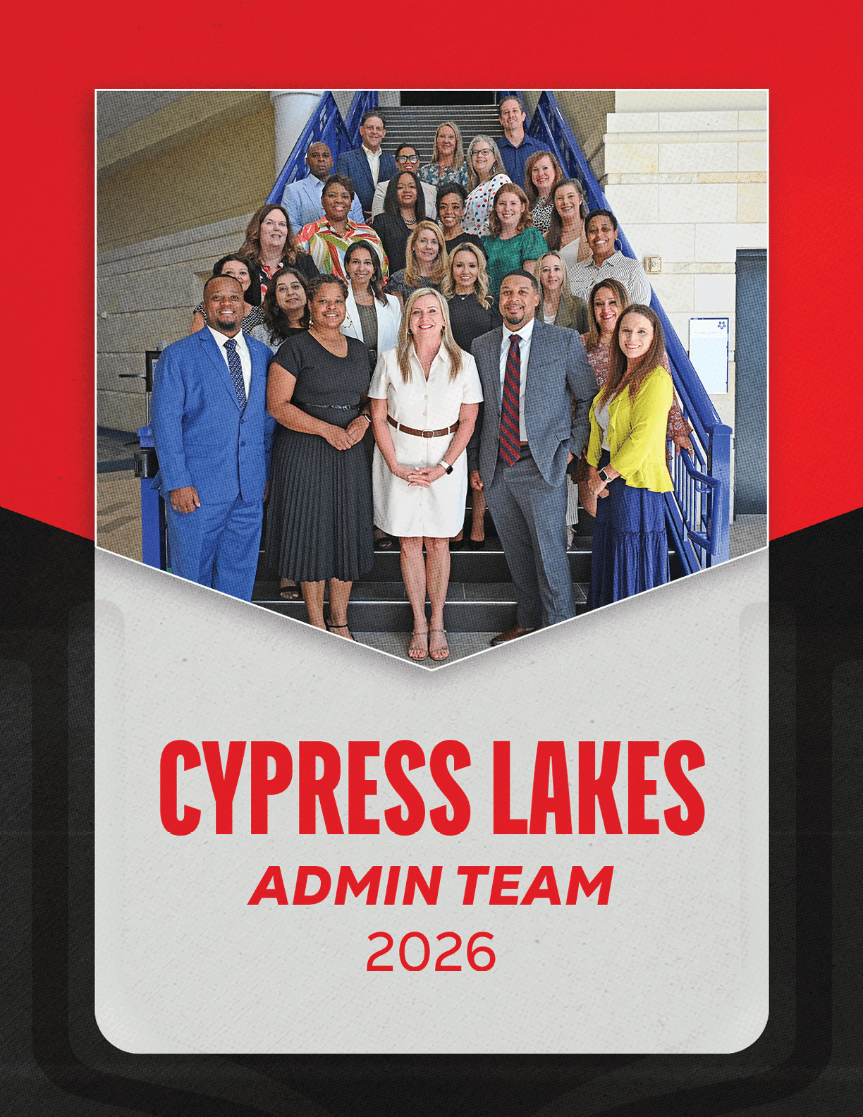 A group of adults dressed in business and casual attire pose on stairs inside a building with a sign below reading Cypress Lakes Admin Team 2026. Description generated by AI