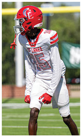 A person wearing a red football helmet and a white jersey with red lettering and the number 15 is looking downward on a sports field. Description generated by AI