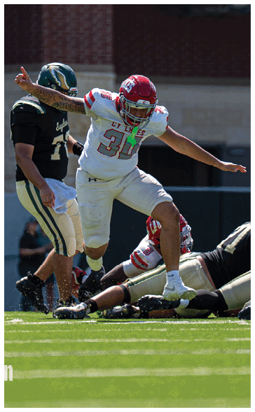 Two football players in action on the field with one wearing a white and red uniform and the other in a black and green uniform. Description generated by AI