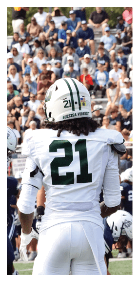 A football player is kneeling on the field, wearing a green jersey and a helmet. AI generated content