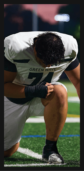 A football player is kneeling on the field, wearing a green jersey and a helmet. AI generated content
