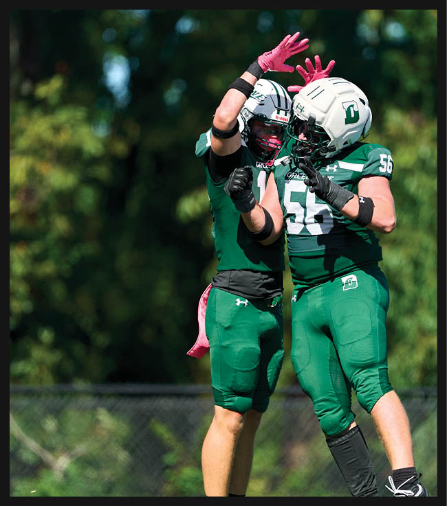 A football game is in progress with players on the field. One player is throwing a football while another player is trying to catch it. The players are wearing uniforms and are actively engaged in the game. AI generated content
