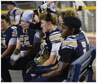 A group of young men are sitting on a bench, wearing football uniforms. AI generated content
