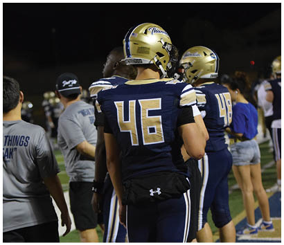 A group of football players wearing blue and gold uniforms are standing on a field. AI generated content