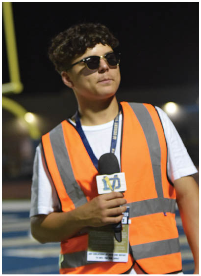 A man wearing an orange vest and sunglasses stands on a field. AI generated content