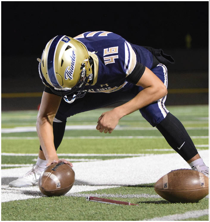 A football player is bending over to pick up a football on a field at night. AI generated content