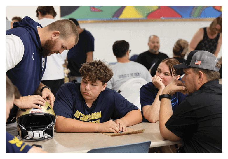 A group of people are sitting around a table, with a man in a blue shirt looking at a piece of paper. Another man is showing him something on the table. AI generated content