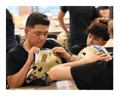 A man is sitting at a table with a group of people, wearing a football helmet. AI generated content