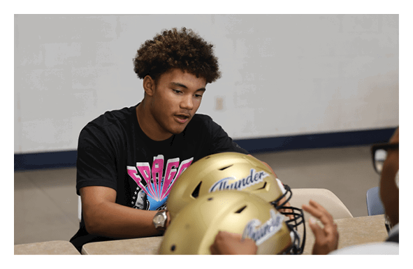 A young man is sitting at a table with a football helmet in front of him. AI generated content