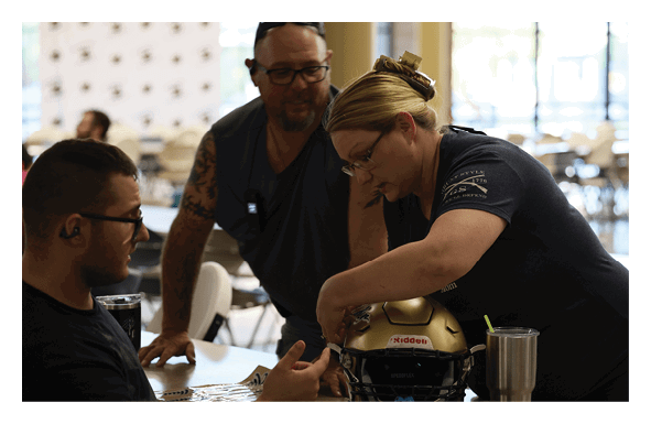 A woman is adjusting a football player's helmet while he sits at a table. AI generated content