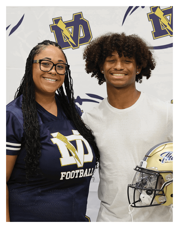 A man and woman are standing in front of a football field banner. The man is holding a football helmet. AI generated content