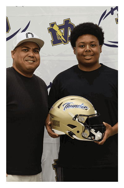 Two men are standing in front of a football backdrop. One of them is holding a football helmet. AI generated content
