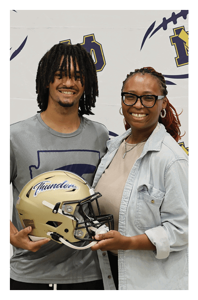 A man and a woman pose together in front of a football backdrop. The man is holding a football helmet. AI generated content