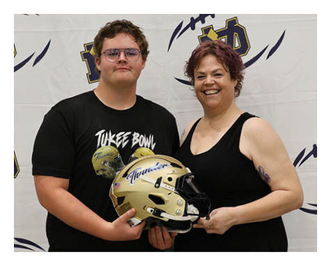 A man and woman are standing in front of a football backdrop. The man is holding a football helmet. AI generated content