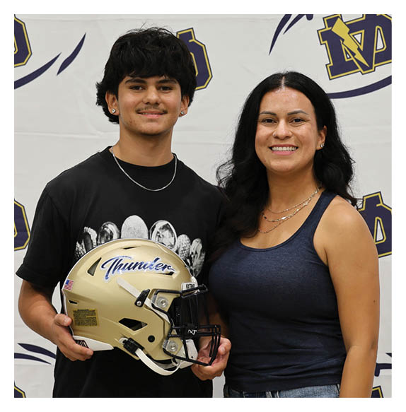 A young man and woman are standing in front of a football banner. The man is holding a football helmet. AI generated content