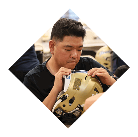A man is sitting at a table with a group of people, wearing a football helmet. AI generated content