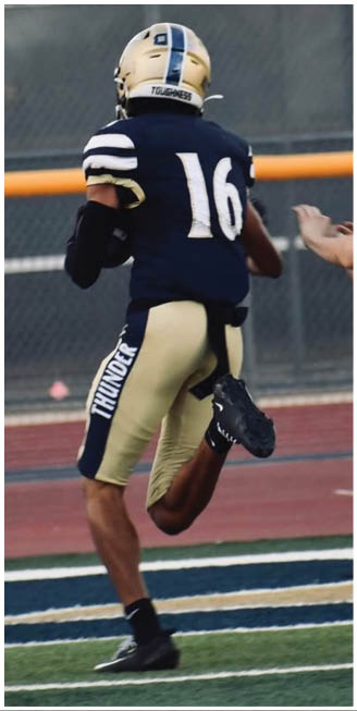 Two people in football uniforms are running on a field with one person chasing the other near the end zone. Description generated by AI