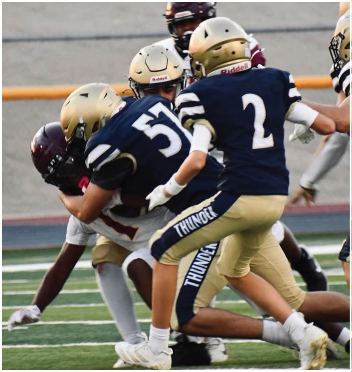 Several adults in football uniforms are engaged in a play on a field, with some players wearing navy blue and gold uniforms labeled “THUNDER" and others in maroon and white. Description generated by AI