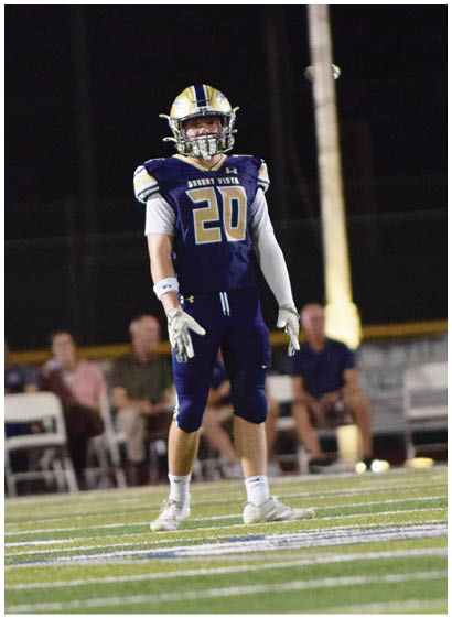 A person in a football uniform with the number 20 stands on a field near the goalpost during a nighttime game. Description generated by AI