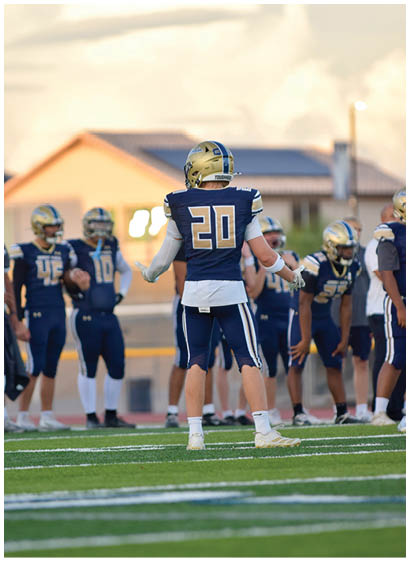 A group of people wearing blue and gold football uniforms are standing on a field with one person in the center facing away from the camera. Description generated by AI