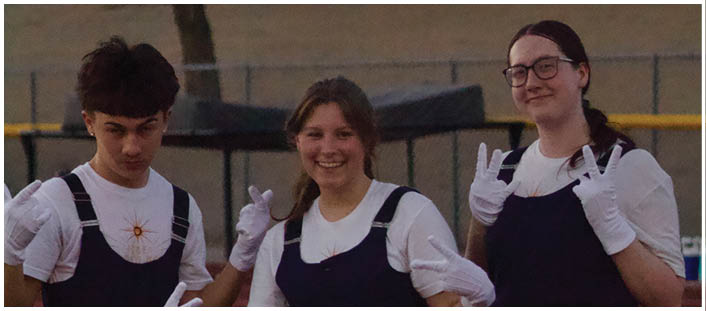 Three people wearing matching dark sleeveless outfits over white shirts and white gloves are posing with cheerful expressions on a track field. Description generated by AI
