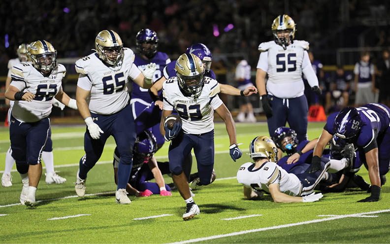 A group of people in football uniforms are actively playing on a field with one person running with the ball while others attempt to block or tackle. Description generated by AI