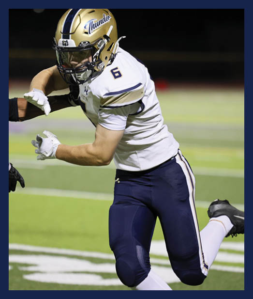 Two people in sports uniforms are engaged in a football game on a green field with white yard lines. Description generated by AI
