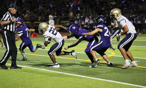 A group of people in football uniforms are actively playing on a field with one person running with the ball while others attempt to tackle or block. Description generated by AI
