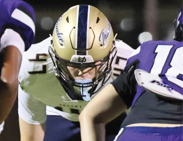 Two people in football uniforms and helmets are facing each other on a field, appearing ready for a play. Description generated by AI