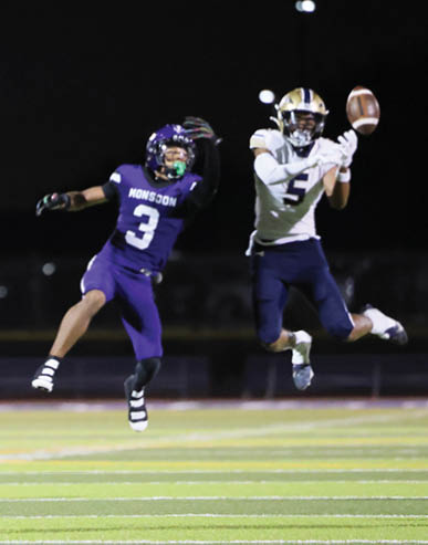 A person in a purple football uniform with the number 3 is jumping to catch a football while two other people in white and navy uniforms are nearby on a football field at night. Description generated by AI