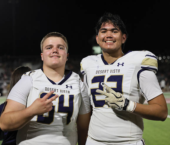 An adult wearing a football uniform with the number 64 is smiling and making a peace sign with their fingers on a sports field at night. Description generated by AI