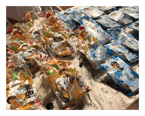 Several clear plastic bags decorated with gingerbread figures and candy cane designs contain photos of people and are arranged on a table covered with a sports-themed tablecloth. Description generated by AI