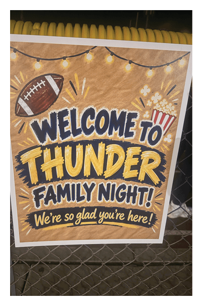 A colorful sign with a football and string lights reads welcome to Thunder Family Night with the message we're so glad you're here. Description generated by AI