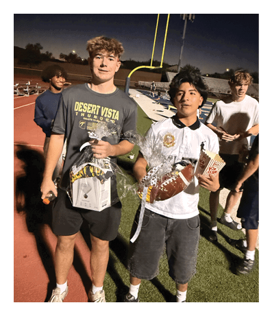 A group of people standing on a sports field at night with one person holding a football and a trophy. Description generated by AI