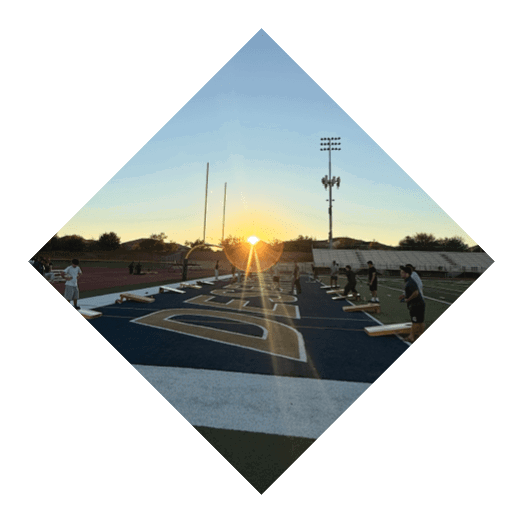 A sunset is visible over a sports field with light poles and a track surrounding the field under a clear sky. Description generated by AI