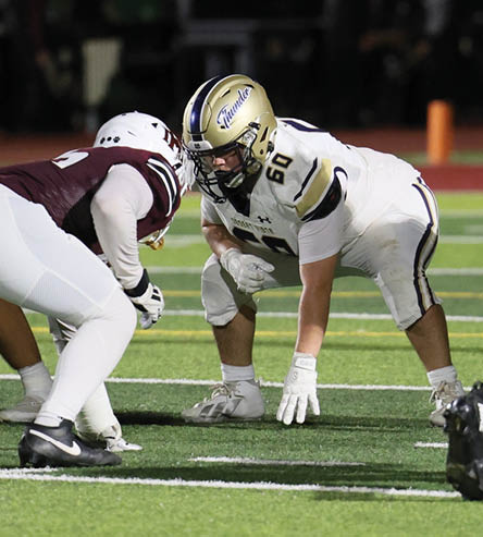 A person wearing a maroon and white football uniform is crouched in a ready position on a football field. Description generated by AI