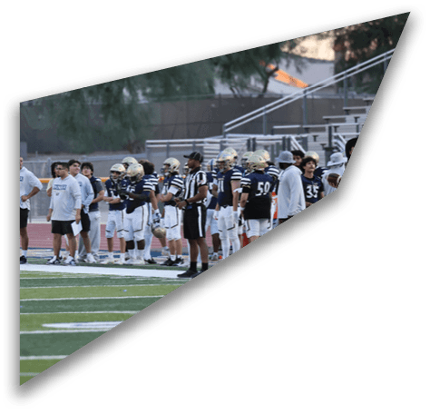 A group of people and a football team in uniform stand on the sidelines of a football field during a game or practice. Description generated by AI