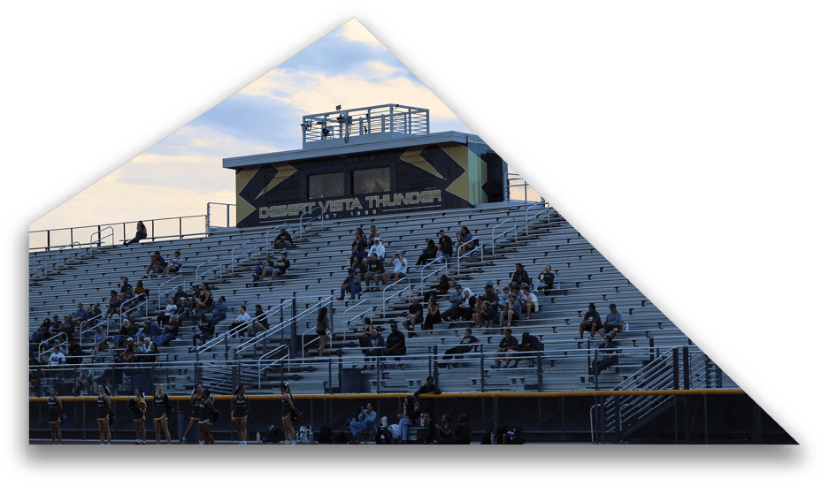 Adults and children are seated sparsely in metal bleachers at an outdoor sports venue under a partly cloudy sky. Description generated by AI