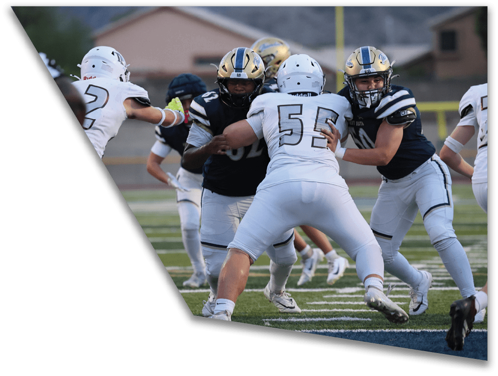 People wearing football uniforms are engaged in a play on a field with some players blocking and others preparing to move. Description generated by AI
