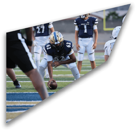 A person in a football uniform is crouched on a field holding a football, preparing to snap it, while other players stand nearby. Description generated by AI