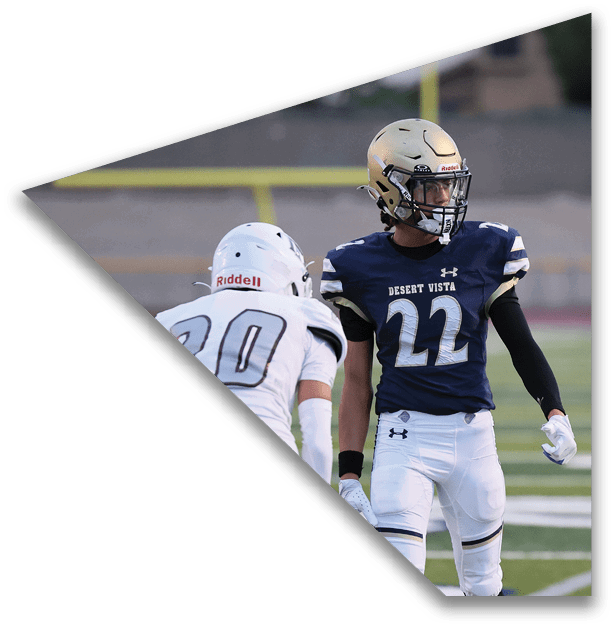 Two people wearing football uniforms and helmets stand on a field, one in a navy blue jersey with the number 22 and the other in a white jersey with the number 20. Description generated by AI