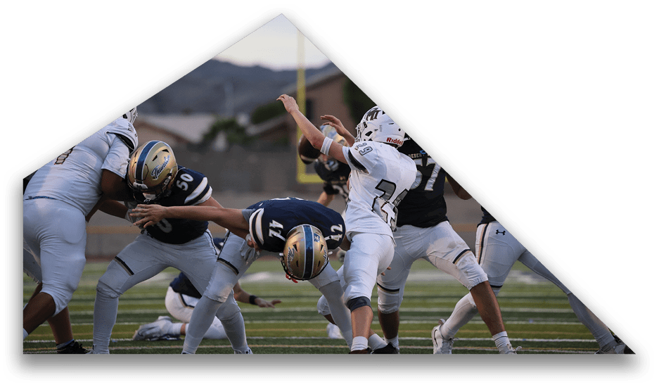 Several people wearing football uniforms are engaged in a dynamic play on a football field with a goalpost and mountains visible in the background. Description generated by AI