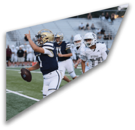 Players in football uniforms are actively engaged in a game on a field with empty bleachers in the background. Description generated by AI