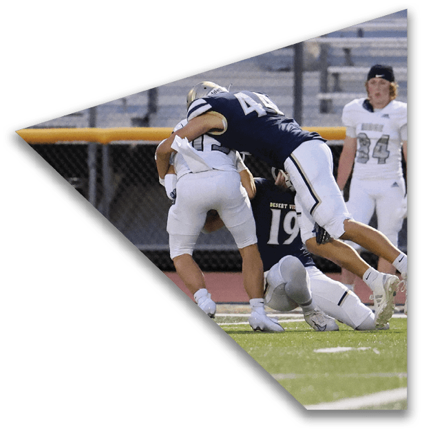 Two people in football uniforms are engaged in a tackle on a field while another person in uniform watches nearby. Description generated by AI