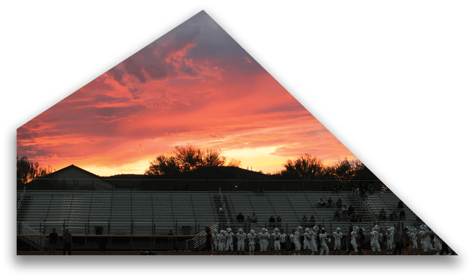 A group of people in sports uniforms stand near the edge of empty bleachers under a vibrant orange and pink sunset sky. Description generated by AI