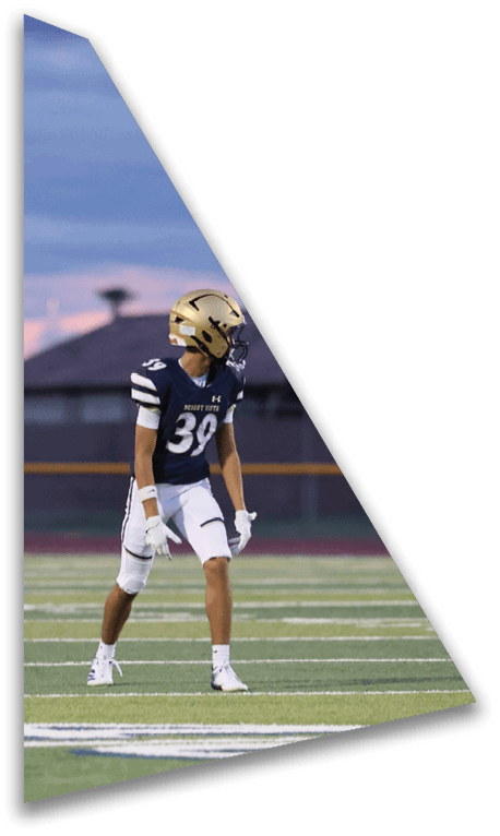 A person wearing a football uniform and helmet stands on a field with a sunset sky in the background. Description generated by AI