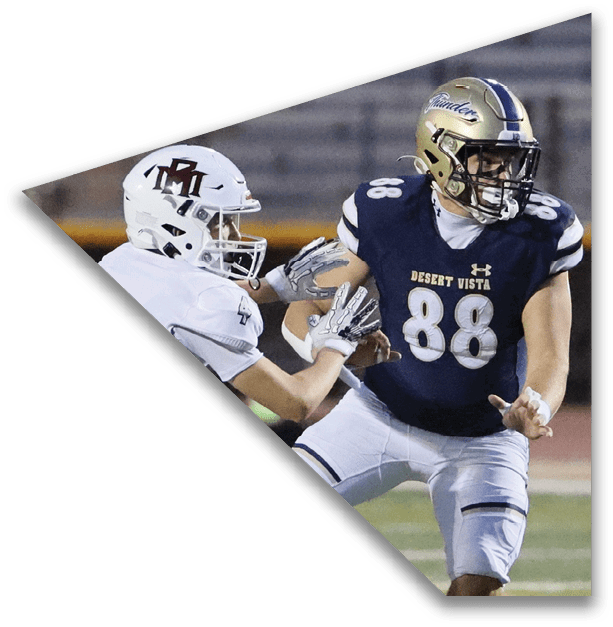 Two people in football uniforms are engaged in a play on a field, with one wearing a dark jersey and helmet and the other in a white jersey and helmet. Description generated by AI