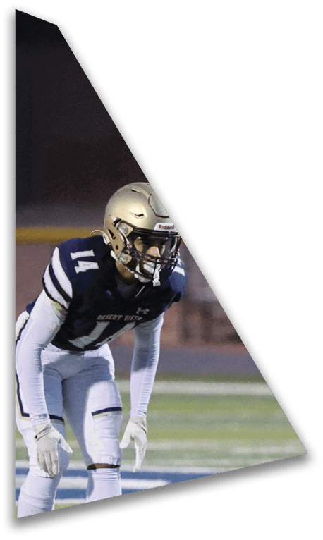 A person wearing a football helmet and uniform is crouched on a field under dark lighting. Description generated by AI