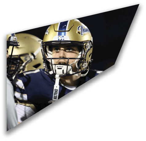 A person wearing a gold football helmet and navy blue uniform with white and gold stripes is looking to the side during a nighttime game. Description generated by AI